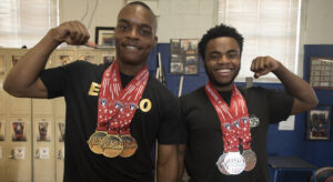 Two young men flexing arms wearing weightlifting medals they have earned